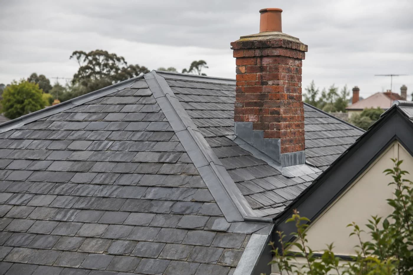 Weathered slate roof tiles and lead flashing beside a brick chimney